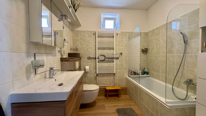A bathroom in a family house with a bathtub, a floor with a wooden decor, and modern elements.