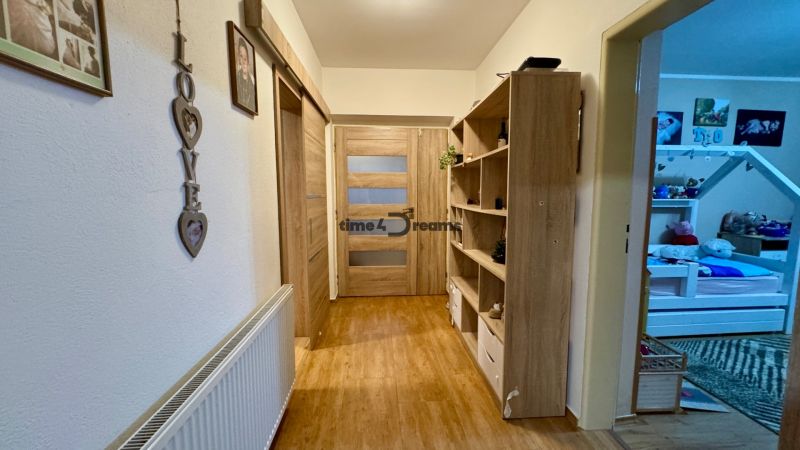A hallway with a wooden decor floor, shelves, and decorations in a family house.