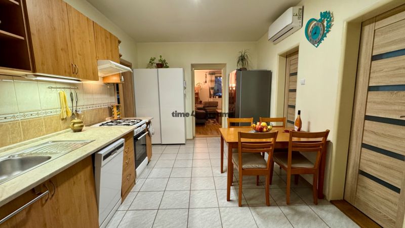 A kitchen in a family house with four chairs, appliances, and a clock on the wall.