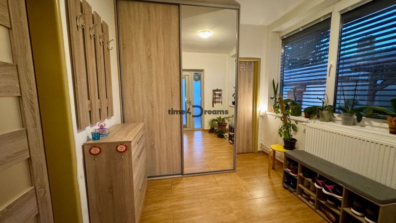 A hallway in a family house with a wooden decor floor, a mirror, and flowers on the windowsill.