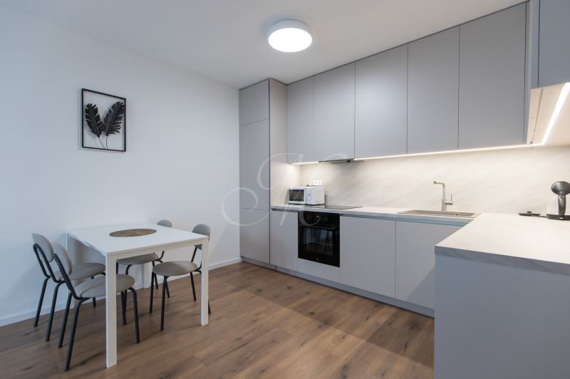 A kitchen in a 2-room apartment with a wooden decor floor, a dining table, and appliances.