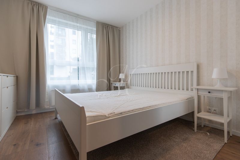 A bright bedroom with white furniture and a wood-patterned floor in a 2-room apartment.