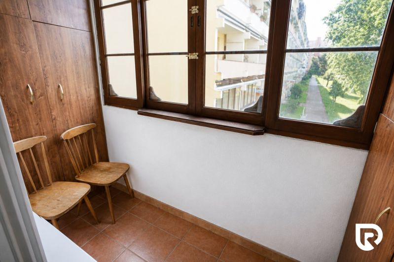 A balcony in a 2-room apartment with a wooden decor and a view of greenery.