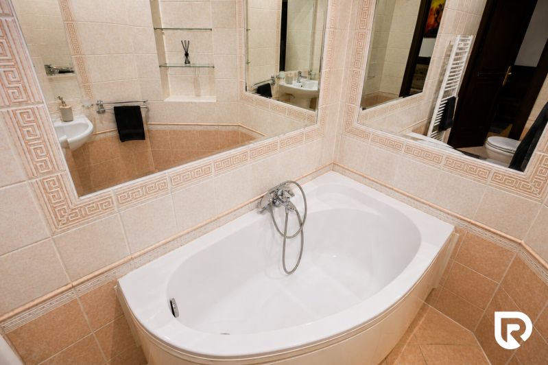 A bathroom with a rounded bathtub and a mirror in a 2-room apartment.
