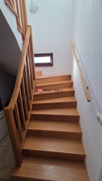 The staircase with a wooden decor leads in the Family house to a small window and a railing.
