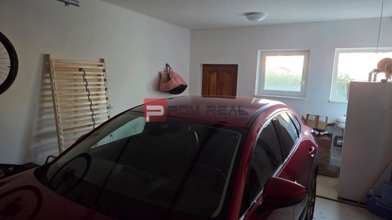 A garage in a family house with a car, windows, and stored items.