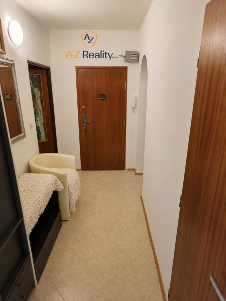 A hallway in a 4-room apartment with tiles, wooden doors, and a light chair.