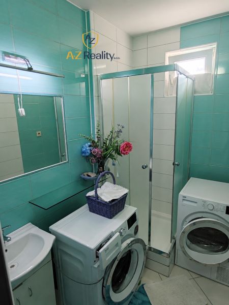 A bathroom in a 4-room apartment with a washing machine, dryer, shower, and decorative flowers.