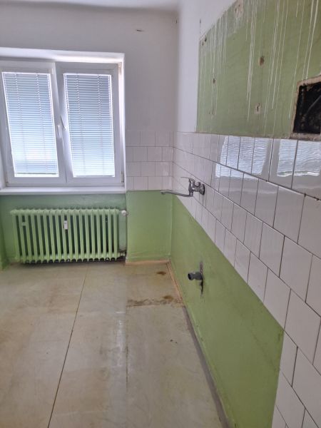 A kitchen in a 2-room apartment with white tiles and green walls.