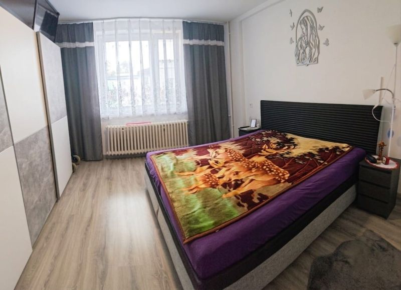 A bedroom in a family house with a wooden decor floor and a bed with a colorful blanket.