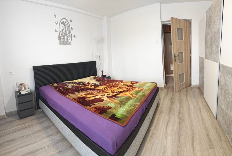 Bedroom in a family house with a bed, colorful throw, and floor with wood decor.