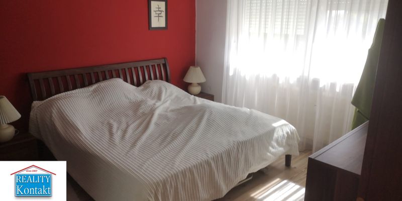A bedroom in a studio apartment with a red wall, a bed, and two lamps.