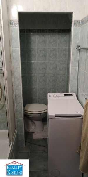 A bathroom in a studio apartment with a washing machine next to the toilet.