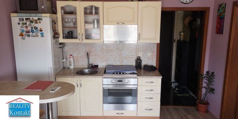 A kitchen in a studio apartment with a kitchen unit, wood decor, and appliances.