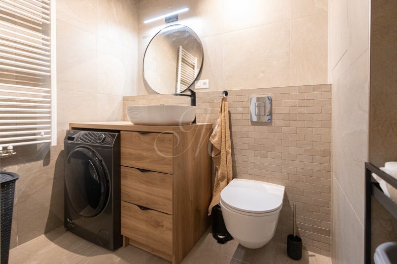 Bathroom with a washing machine in a 2-room apartment, sink on a wooden cabinet, round mirror.