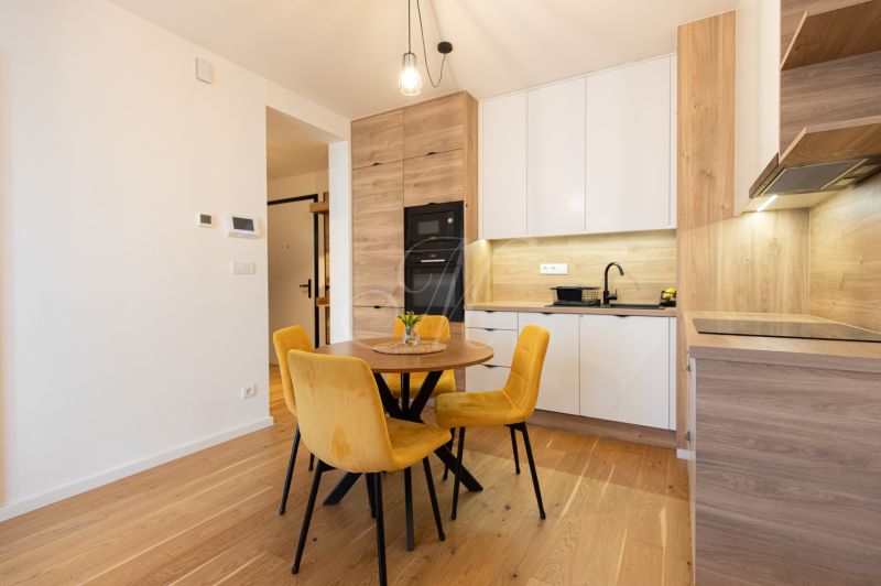 A kitchen in a 2-room apartment with a wooden decor floor and yellow chairs.