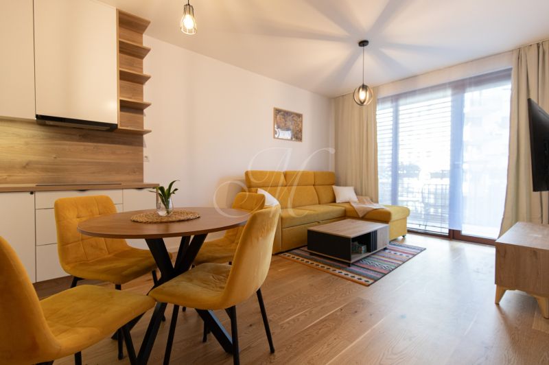Living room in a two-room apartment with a wooden decor floor and a yellow sofa.