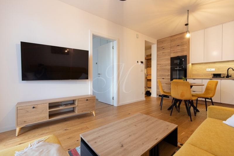 A living room in a two-room apartment with a yellow couch and a wooden decor floor.