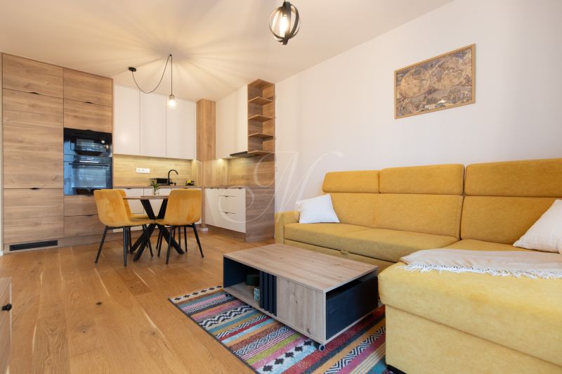 2-room apartment with wood-patterned flooring, yellow sofa, dining table, and kitchen.