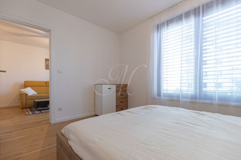 Bedroom with wood-patterned flooring and a view of the neighboring room in a 2-room apartment.