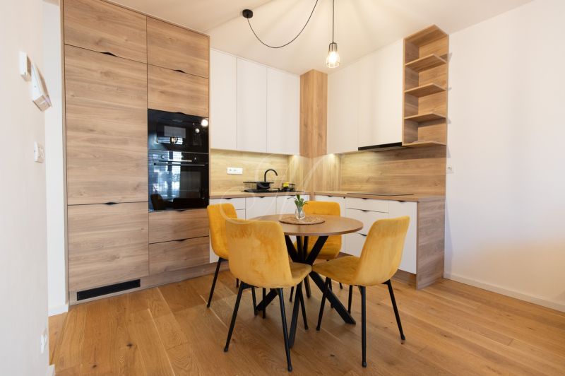 A kitchen in a 2-room apartment with a wooden decor floor and yellow chairs.