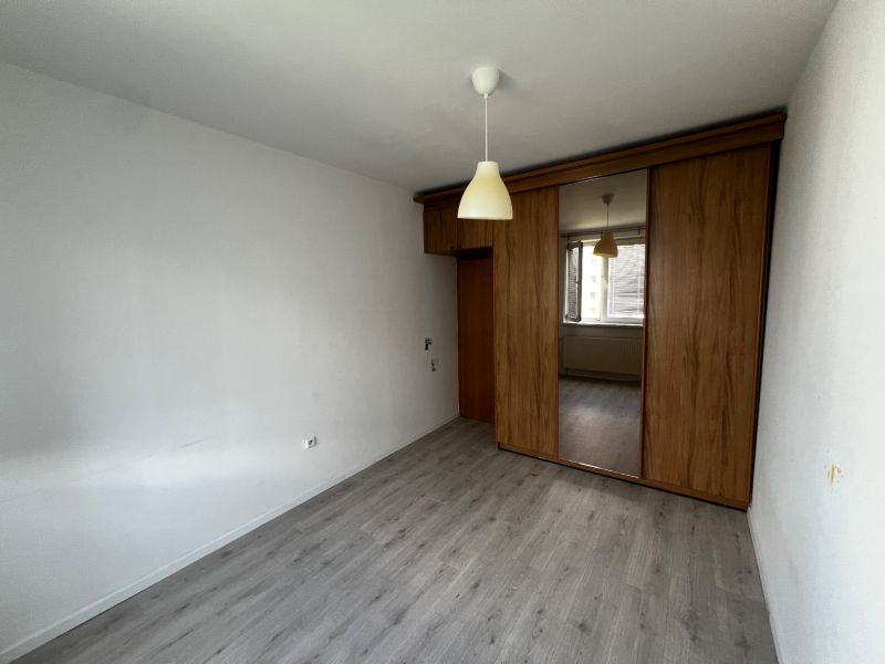 Bedroom with wood-patterned flooring and a built-in wardrobe in a three-room apartment.