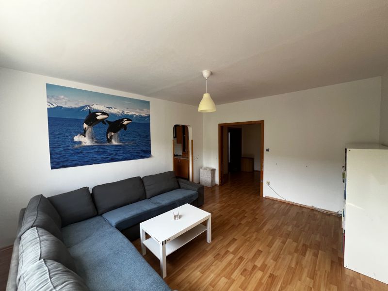 Living room of a three-room apartment with a wooden decor floor and a large sofa.