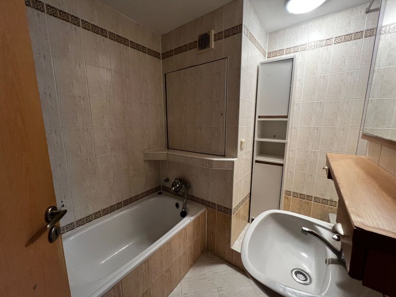 A bathroom in a 3-room apartment with a bathtub, sink, and light tiles.