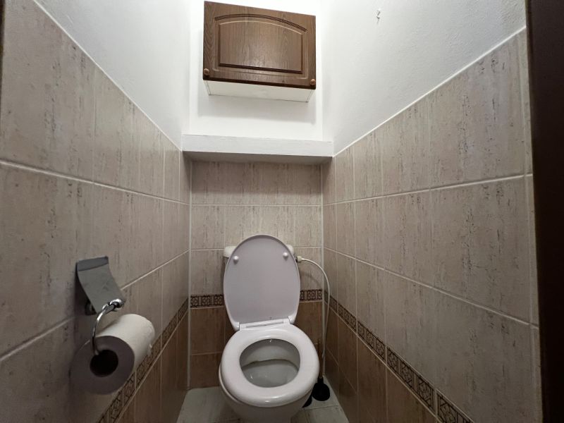 A toilet in a 3-room apartment with tiles and a storage cabinet.