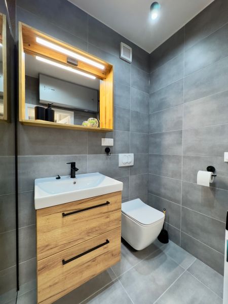 Bathroom in a 2-room apartment with tiles, a mirror, and a sink with wooden decor.