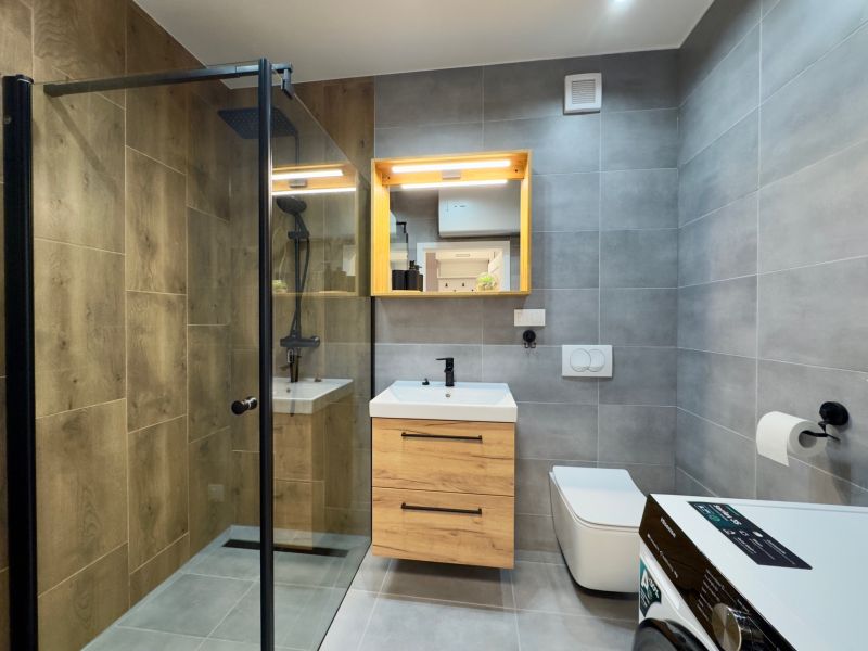 Bathroom in a 2-room apartment with a wooden decor floor and a shower corner.