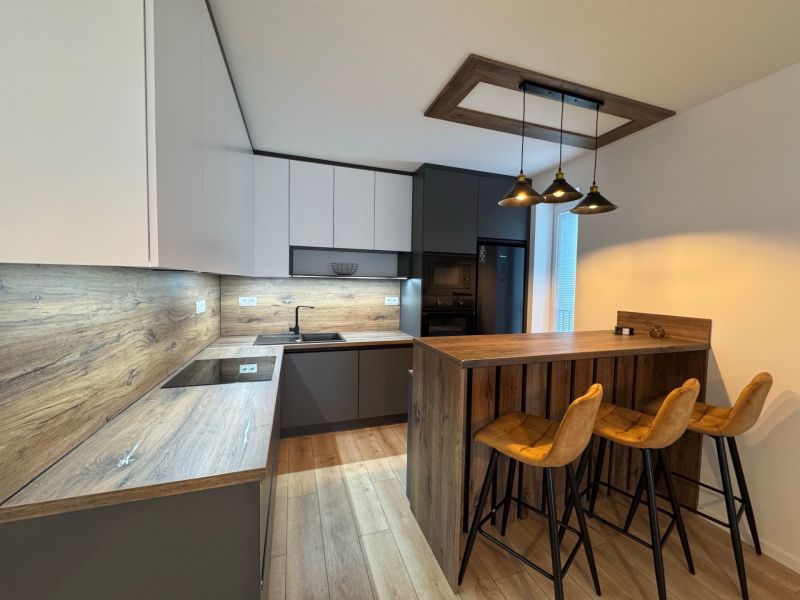 A kitchen in a 2-room apartment with a bar counter, a wooden decor floor, a trio of chairs.