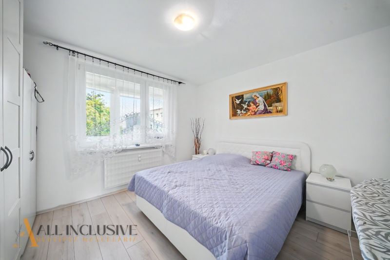 A bright bedroom with wood-patterned flooring and a bed in a three-room apartment.