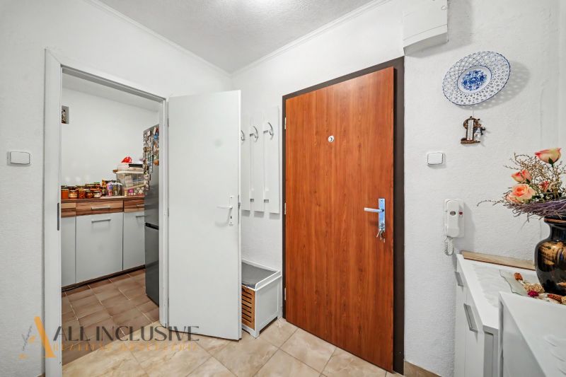 The entrance hall with light walls and a wooden decor floor leads to the kitchen.