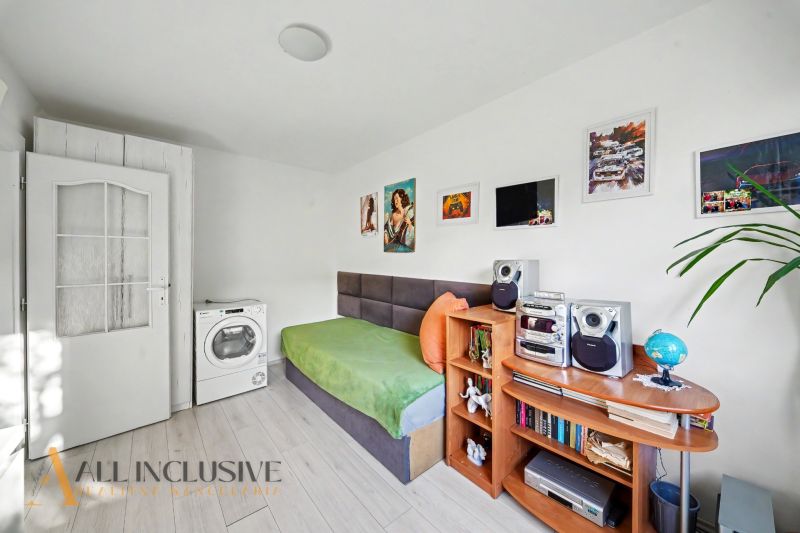 A room in a 3-room apartment with a single bed, a washing machine, and shelves. Floor with wood decor.