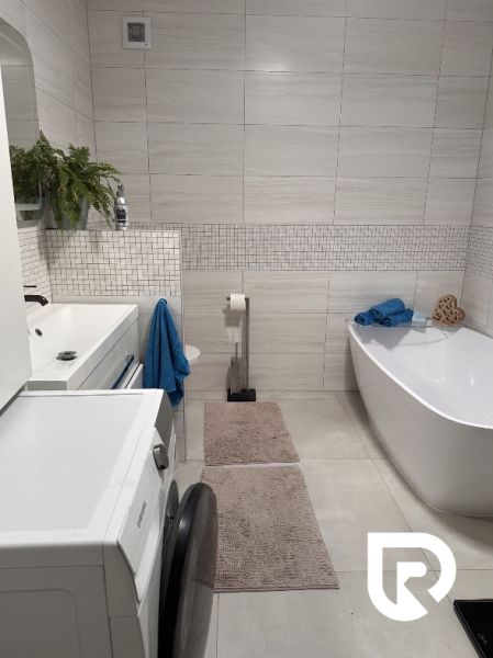 A bathroom in a family house with a washing machine, a bathtub, and white tiles on the walls.