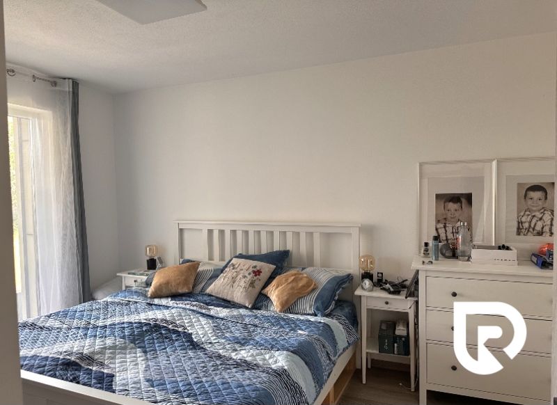 Bedroom in a family house with a bed and a drawer table, light walls and textiles.