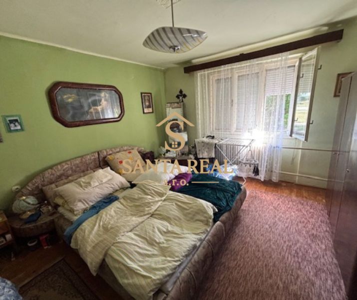 A bedroom in a family house with green walls, a carpet, a bed, and a large window.