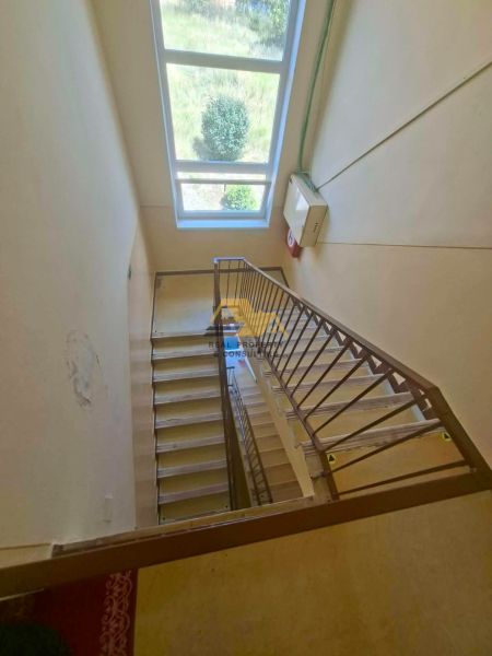 A staircase in a 3-room apartment with a large window providing an outside view.