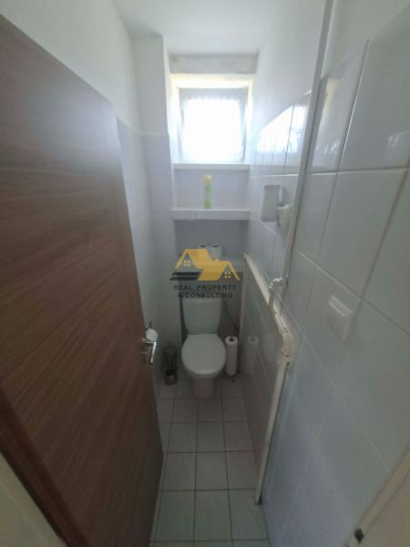 Bathroom with toilet and window in a 3-room apartment. Narrow dimensions, white tiles.