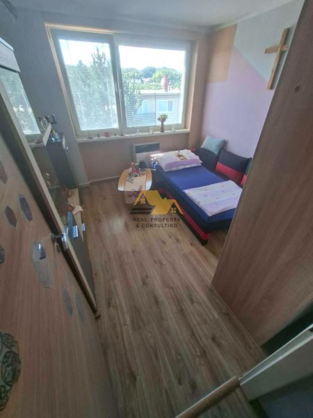 A room in a 3-room apartment with a wood-decor floor and a sofa by the window.