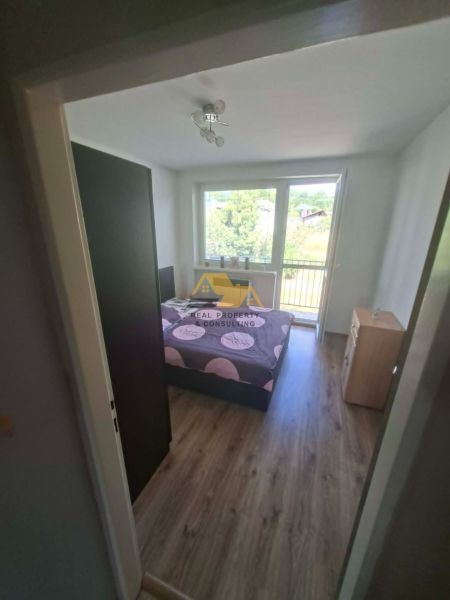 Bedroom in a 3-room apartment with a bed, wood-decorated floor, and a view outside.