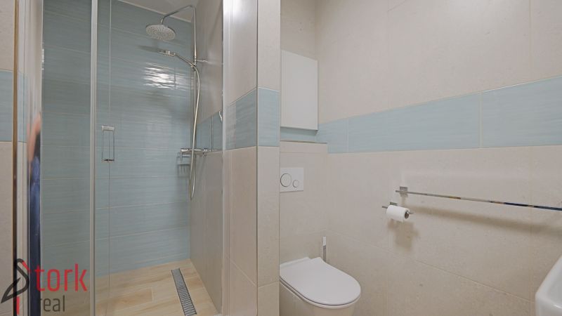 Bathroom in a studio apartment with a modern shower, light tiles, and a toilet.