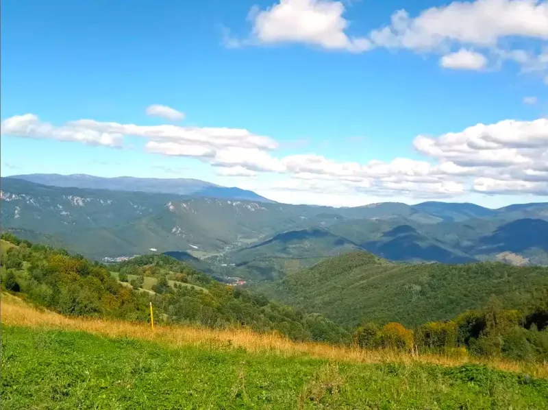 Hilly landscape of agricultural and forest land in Ratkovské Bystré under a blue sky.