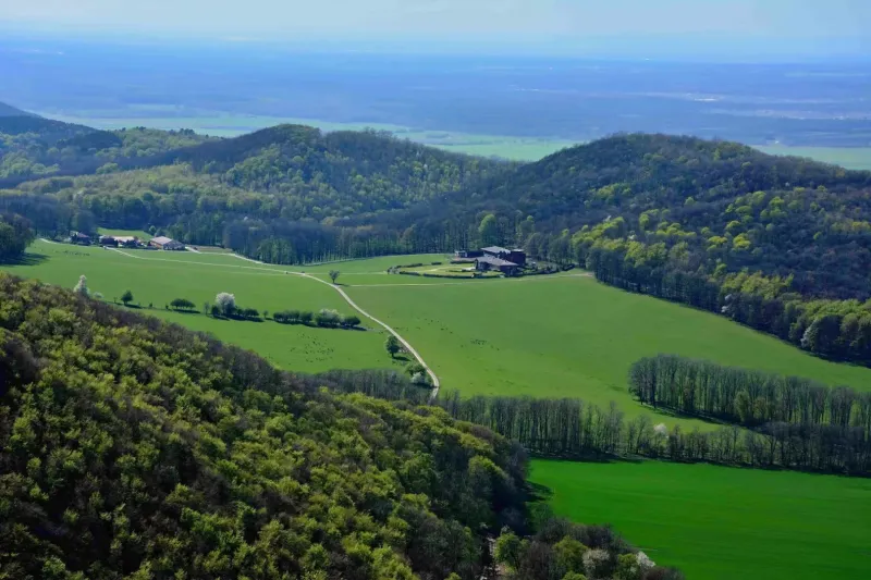 Green agricultural and forest lands around Plavecký Peter with hills and a farm.