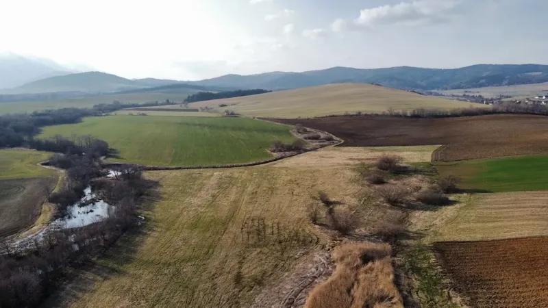 Agricultural and forest lands in Podhorany with diverse colors of fields and low hills.