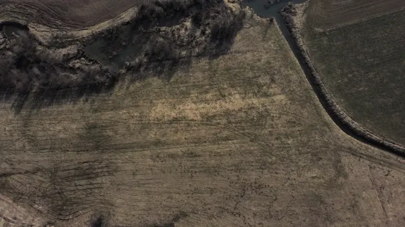 Aerial view of agricultural and forest lands in Podhorany with a river and vegetation.