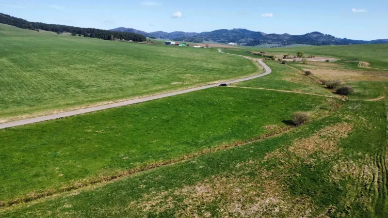 Landscape in Podhorany with agricultural and forest land, a road, and mountains in the background.