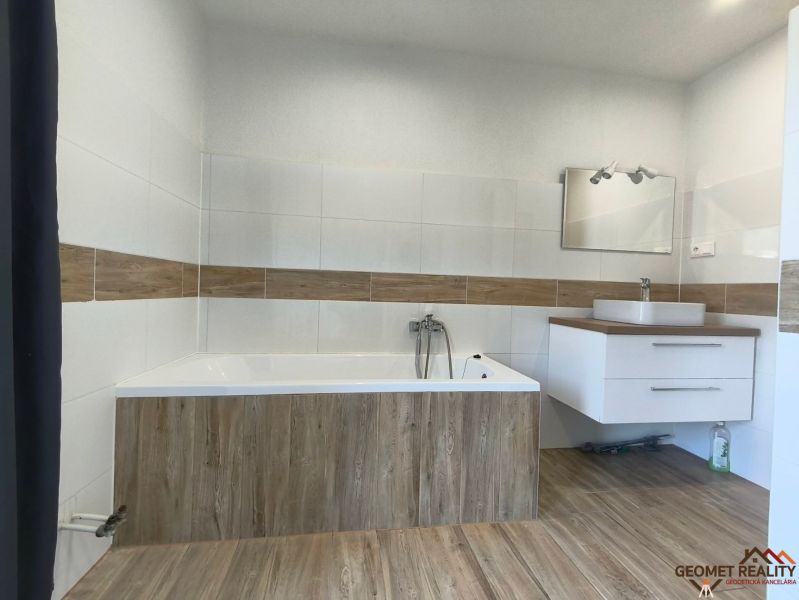 A bathroom with a bathtub, sink, and wooden decor flooring in a family house.