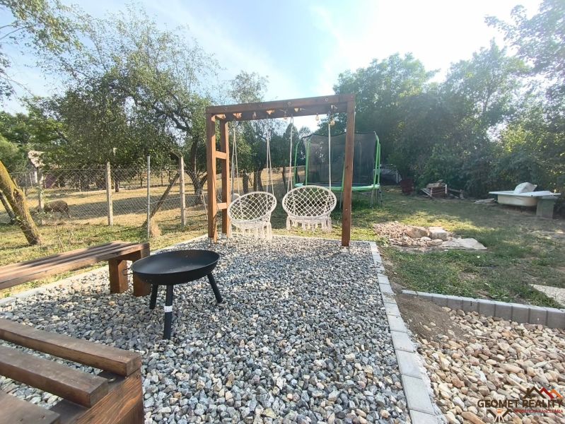 The garden of a family house in Dobroč with a swing, a fireplace, and a trampoline on a stone surface.